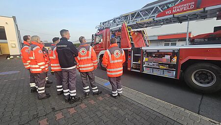 Sanitäter und eine Sanitäterin stehen vor einem Feuerwehrfahrzeug
