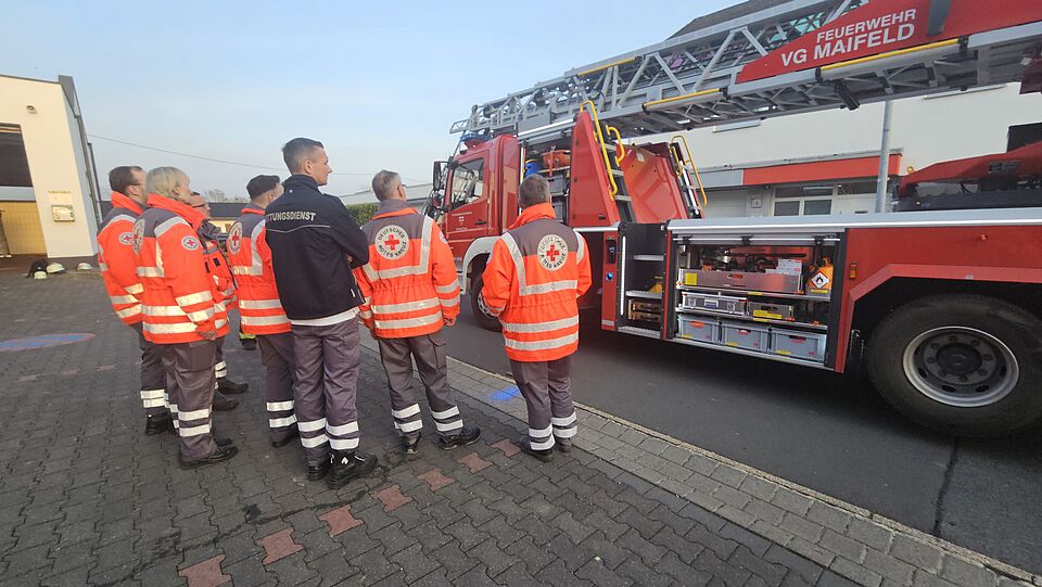 Sanitäter und eine Sanitäterin stehen vor einem Feuerwehrfahrzeug